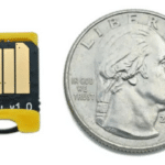 The Bitmerse Romu next to a coin, highlighting its ultra-compact $15.5 \times 12\text{ mm}$ form factor designed to fit entirely inside a USB-A port